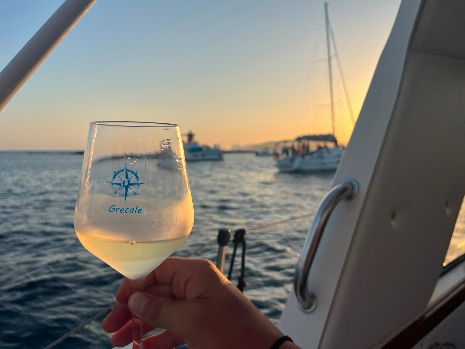 Calice di vino bianco al tramonto a bordo, davanti alla costa di Alghero